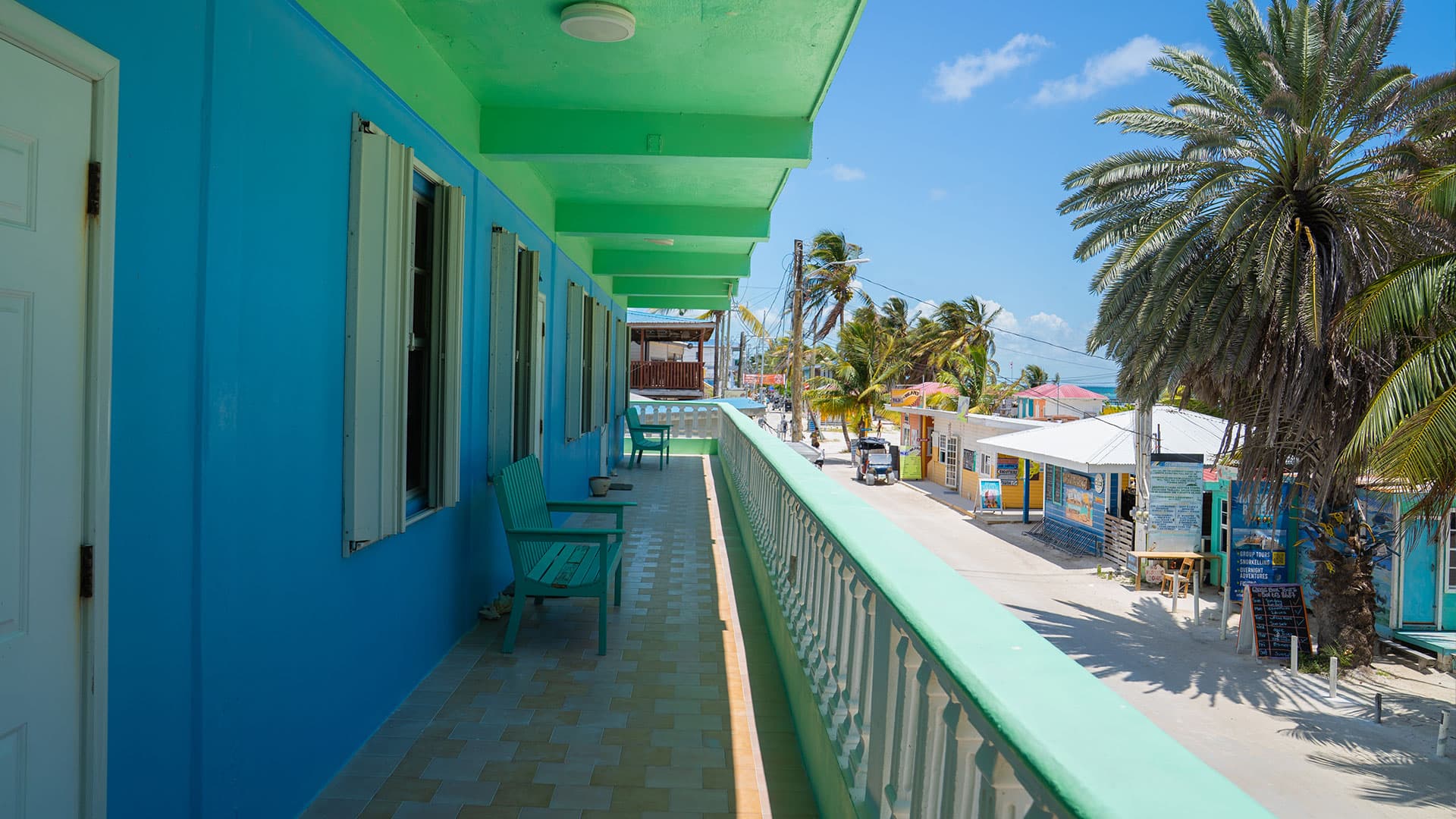 A colorful balcony view overlooking a street lined with palm trees and buildings.